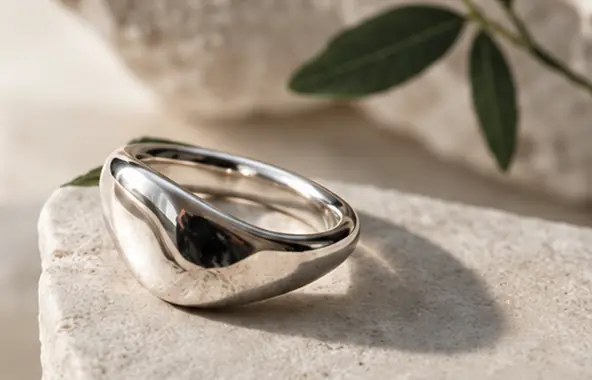 Arc Ring auf einem hellen Steinsockel, mit weichem Licht und Olivenblättern